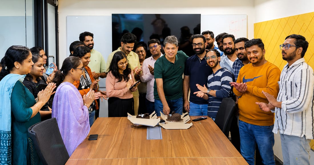 The Onsurity team gathered around a cake celebrating together in a meeting room