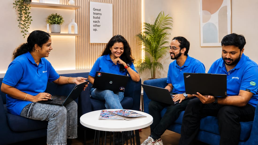 Onsurity teammates talking in the office lounge beneath a “Great teams build each other up” print